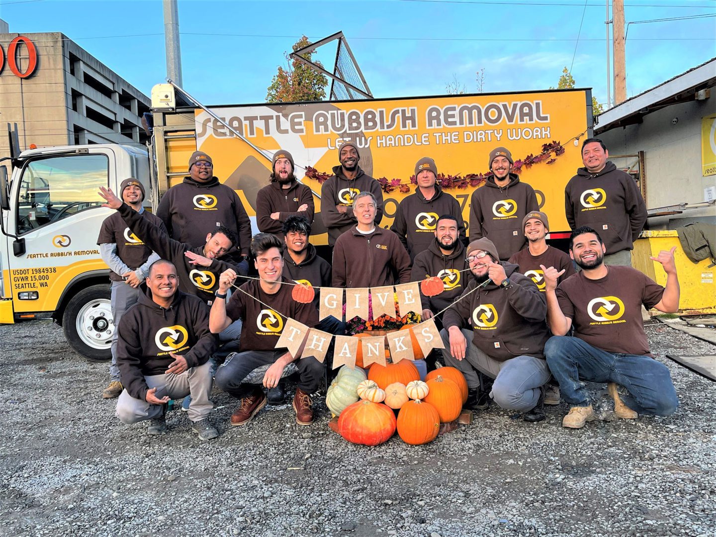 Seattle Rubbish Removal team posing outdoors with pumpkins and a "GIVE THANKS" banner, showcasing their eco-friendly junk removal services in SeaTac.