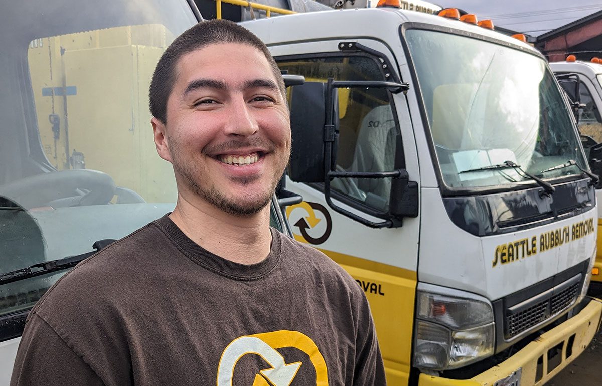 Patrick from the Seattle Rubbish Removal crew smiling in front of company trucks, showcasing team spirit and professionalism in junk removal services.