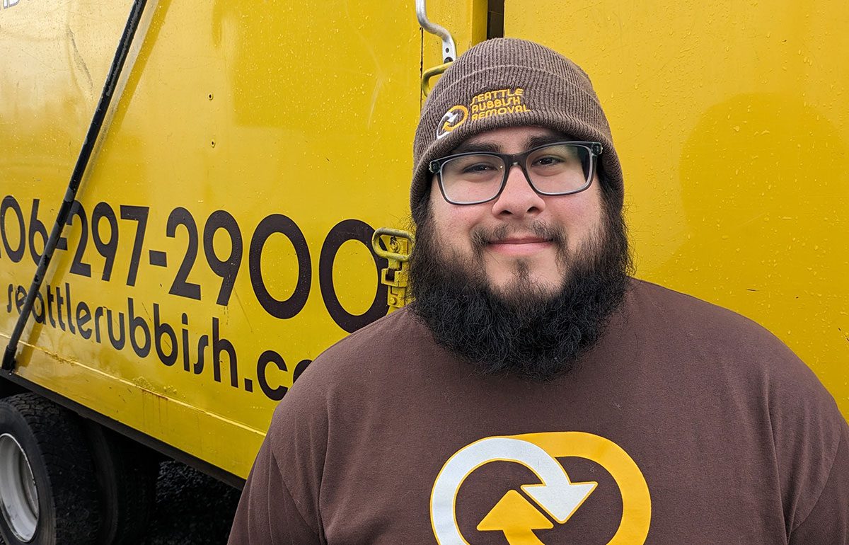 Crew member of Seattle Rubbish Removal smiling in front of a yellow truck displaying the company logo and contact information.