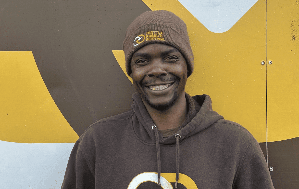 Smiling crew member from Seattle Rubbish Removal wearing a brown beanie and hoodie, against a colorful background featuring the company's logo.